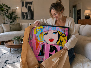 A woman in her living room unwrapping a Dganit Blechner pop-art print from craft paper packaging